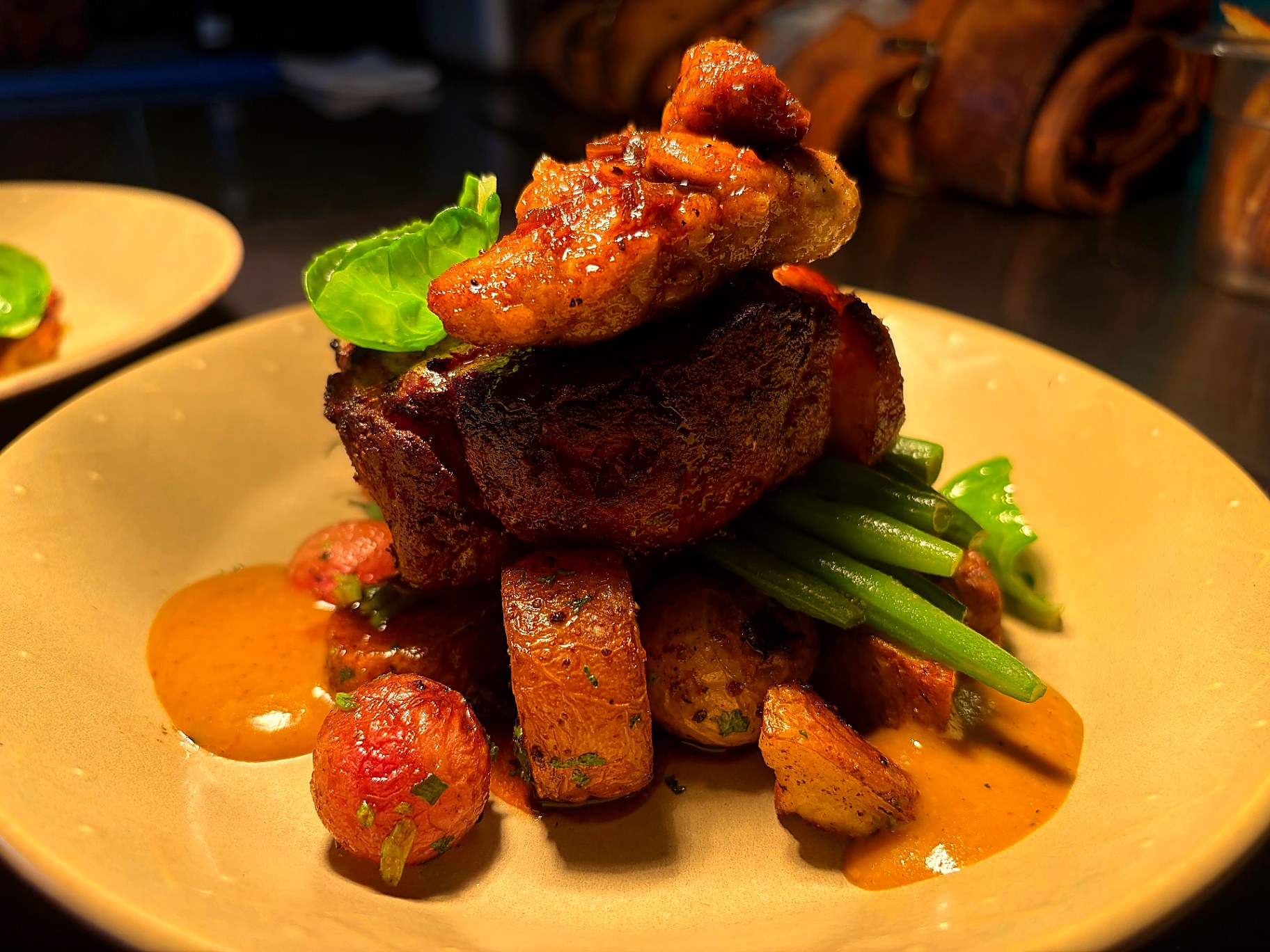 Seared steak stacked over roasted potatoes and green beans with a warm pepper sauce