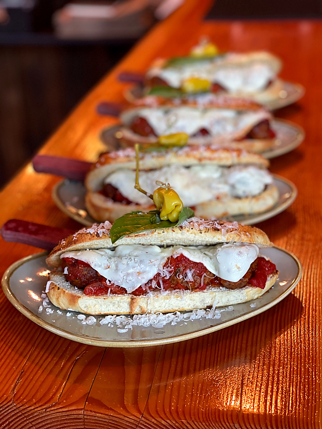 Open-faced meatball subs with melted burrata, marinara, basil and pickled pepper on toasted sourdough
