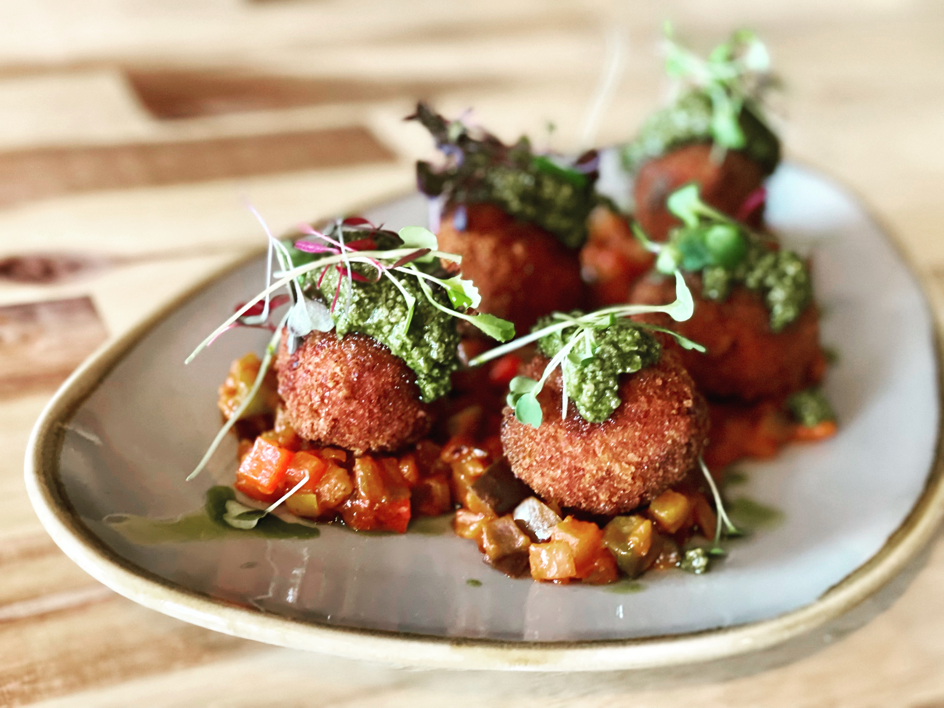 Crispy arancini topped with basil pesto and microgreens, plated over ratatouille